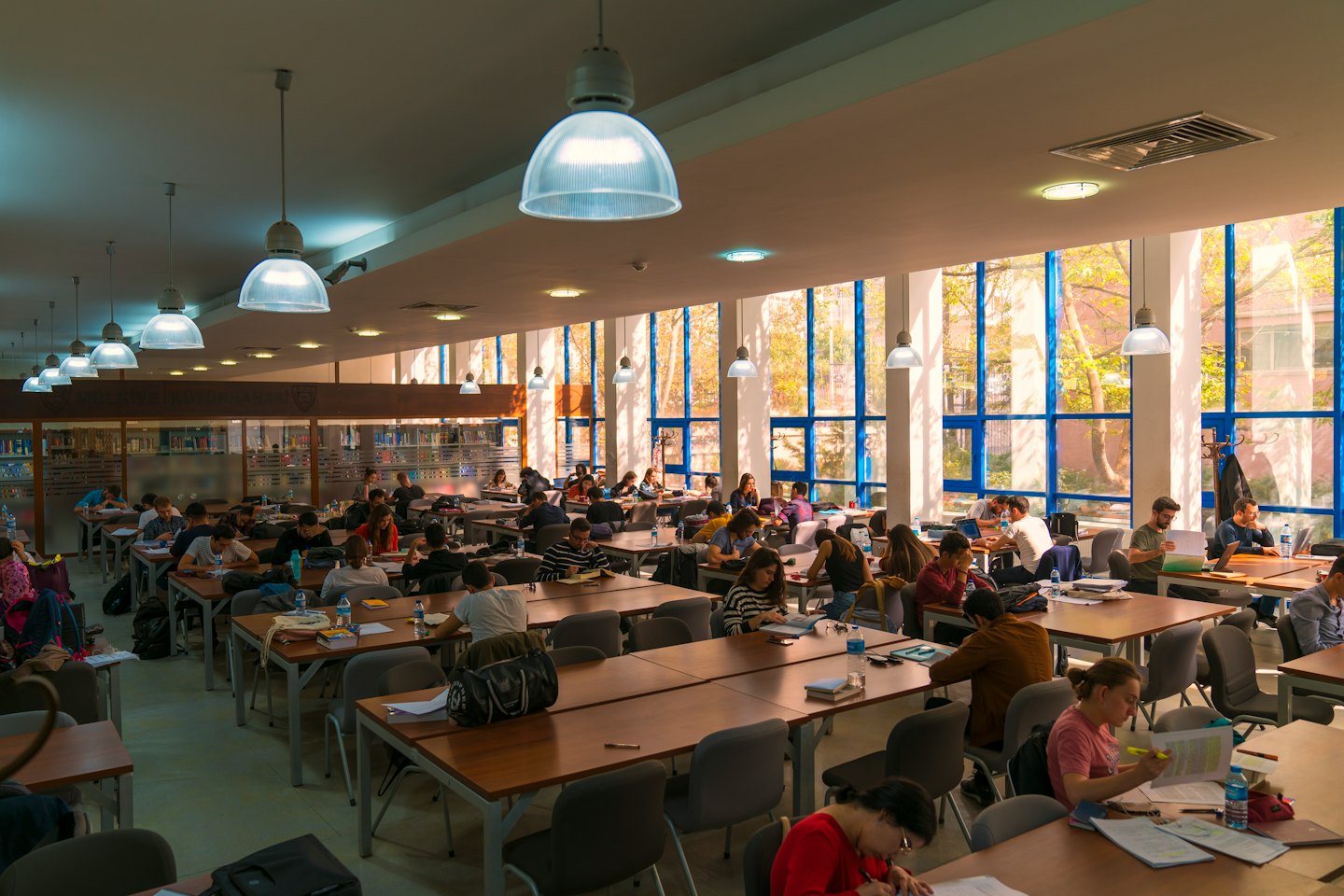 Studenten lernen mit Laptops an Holztischen in einer Bibliothek.